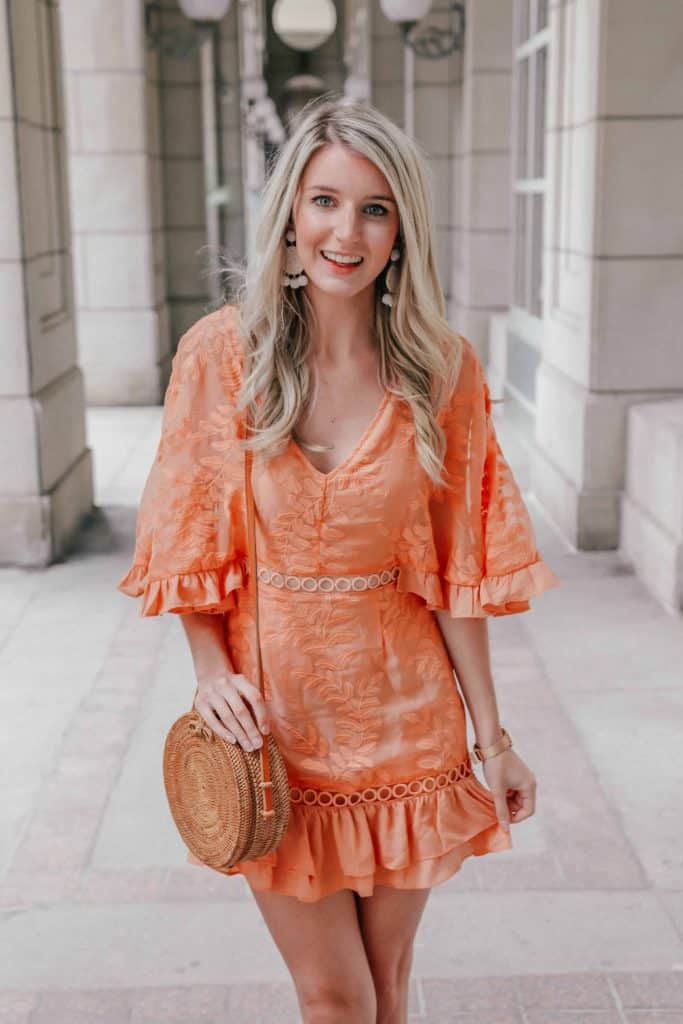 Bright orange coral ruffle dress with a round rattan bag